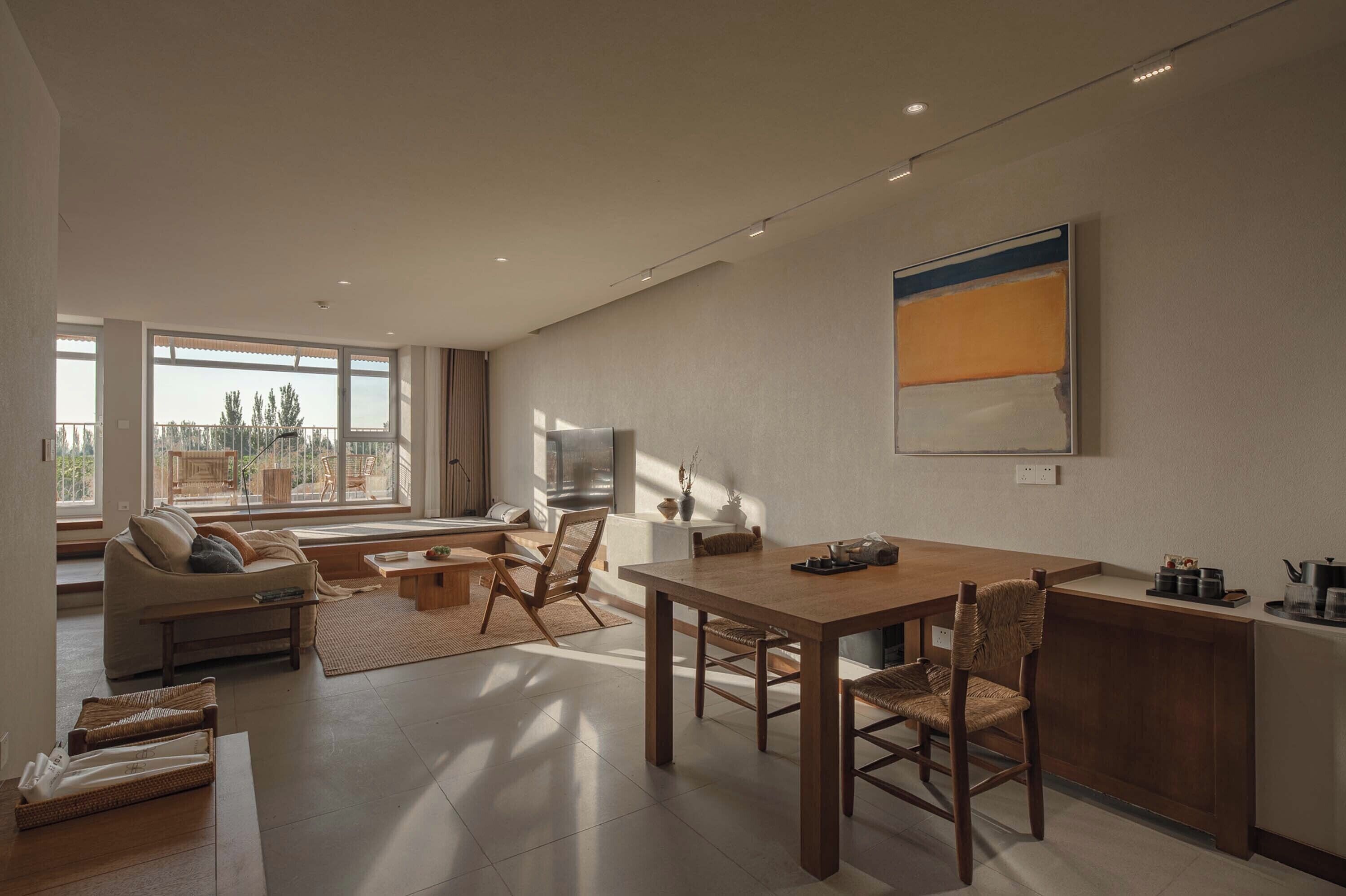 A modern living room with a sofa, coffee table, and dining table. There is a TV on the wall and a window providing natural light.