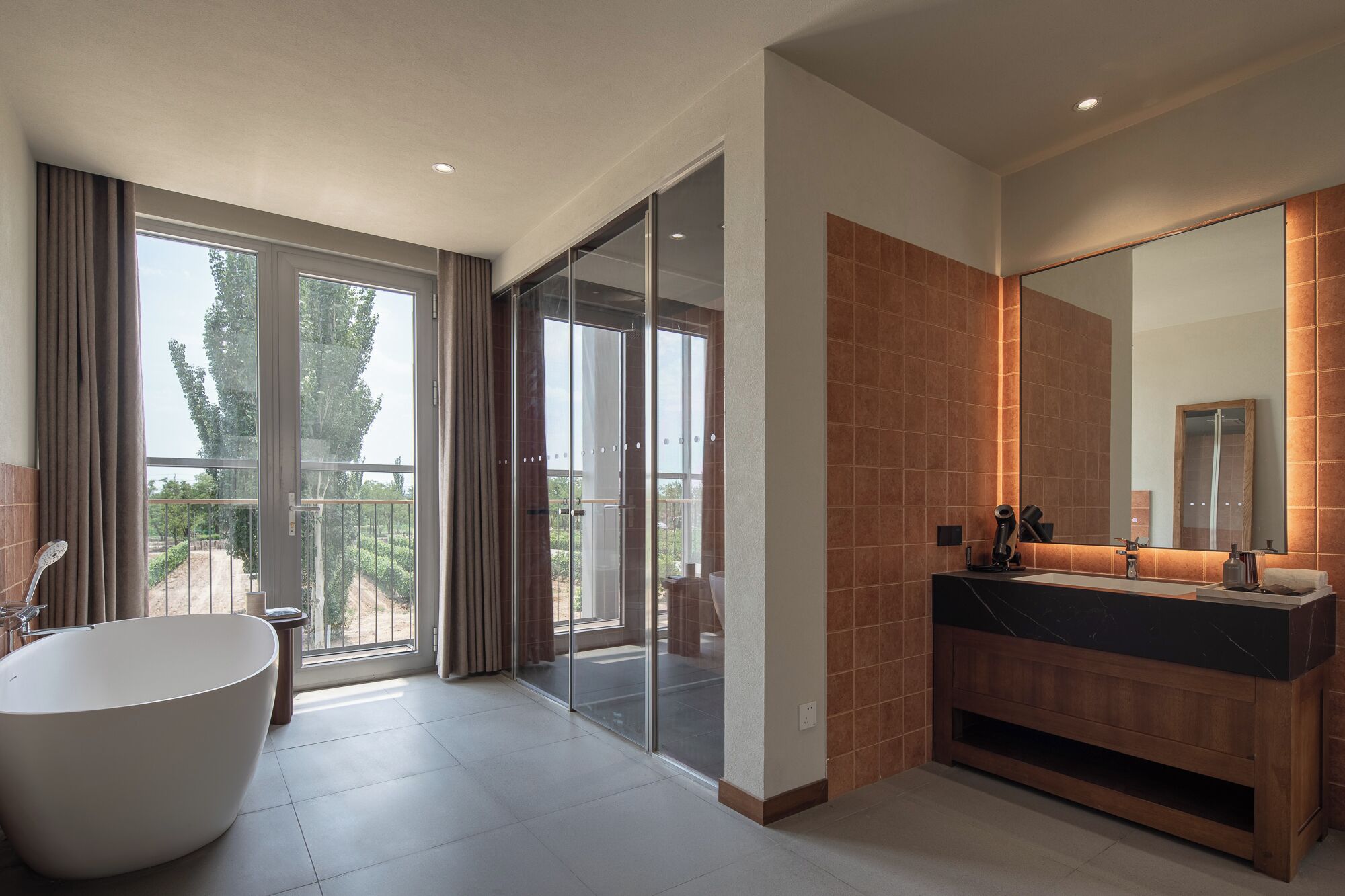 A modern bathroom with a freestanding bathtub, a large mirror, and a vanity with a dark countertop.