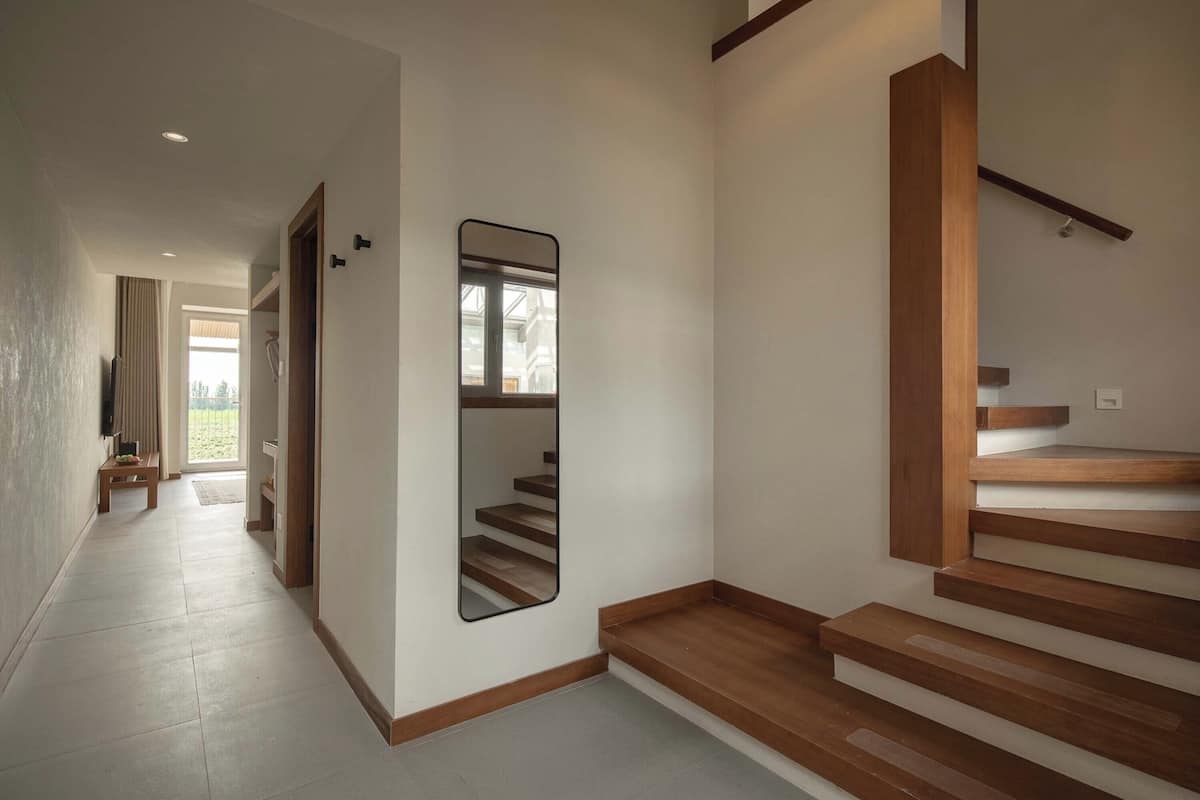 Un pasillo moderno con una escalera de madera, un espejo y una puerta que da a otra habitación.