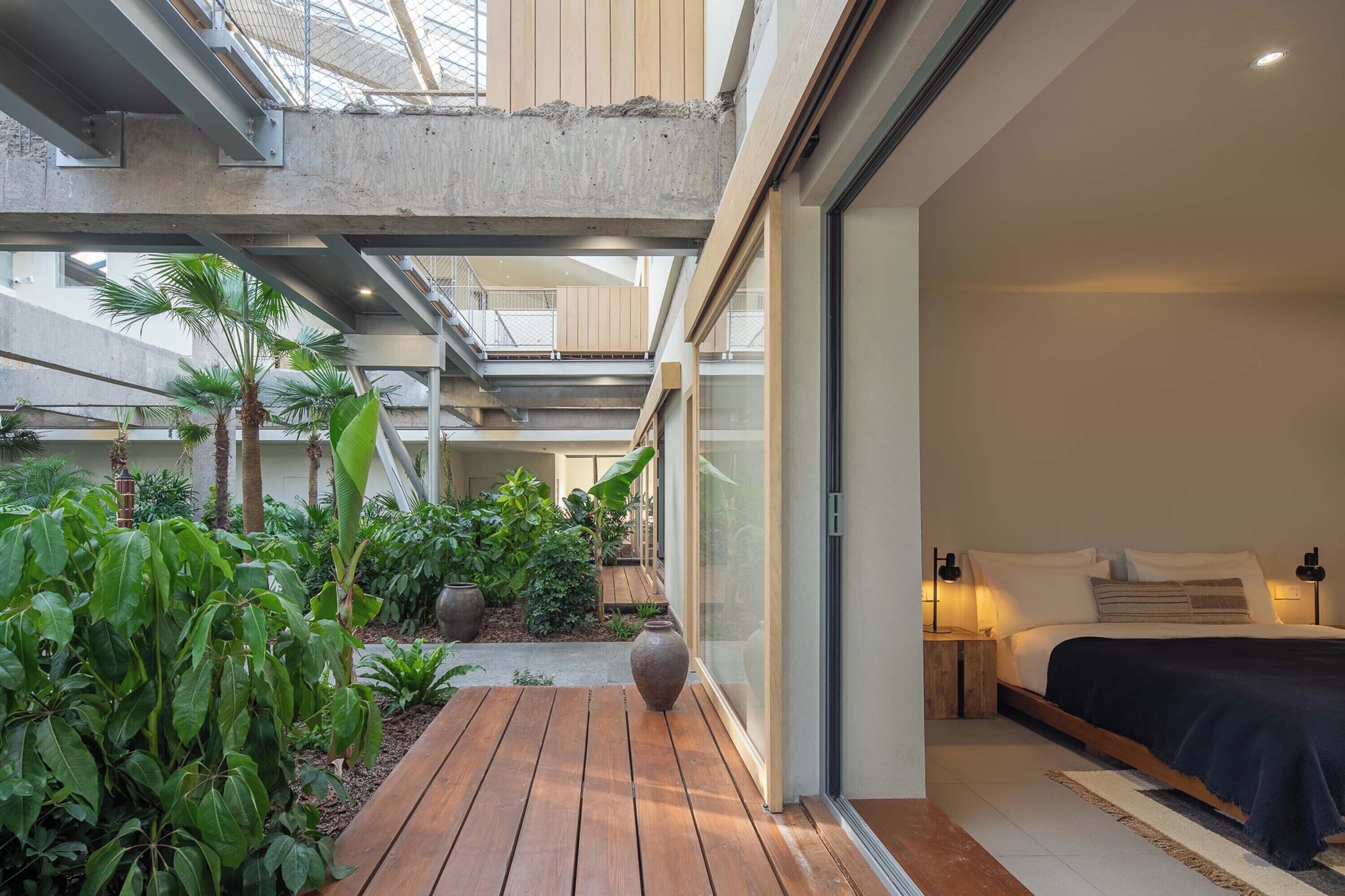 Habitación de hotel moderna con una cama grande, suelo de madera y vistas a un exuberante jardín interior.