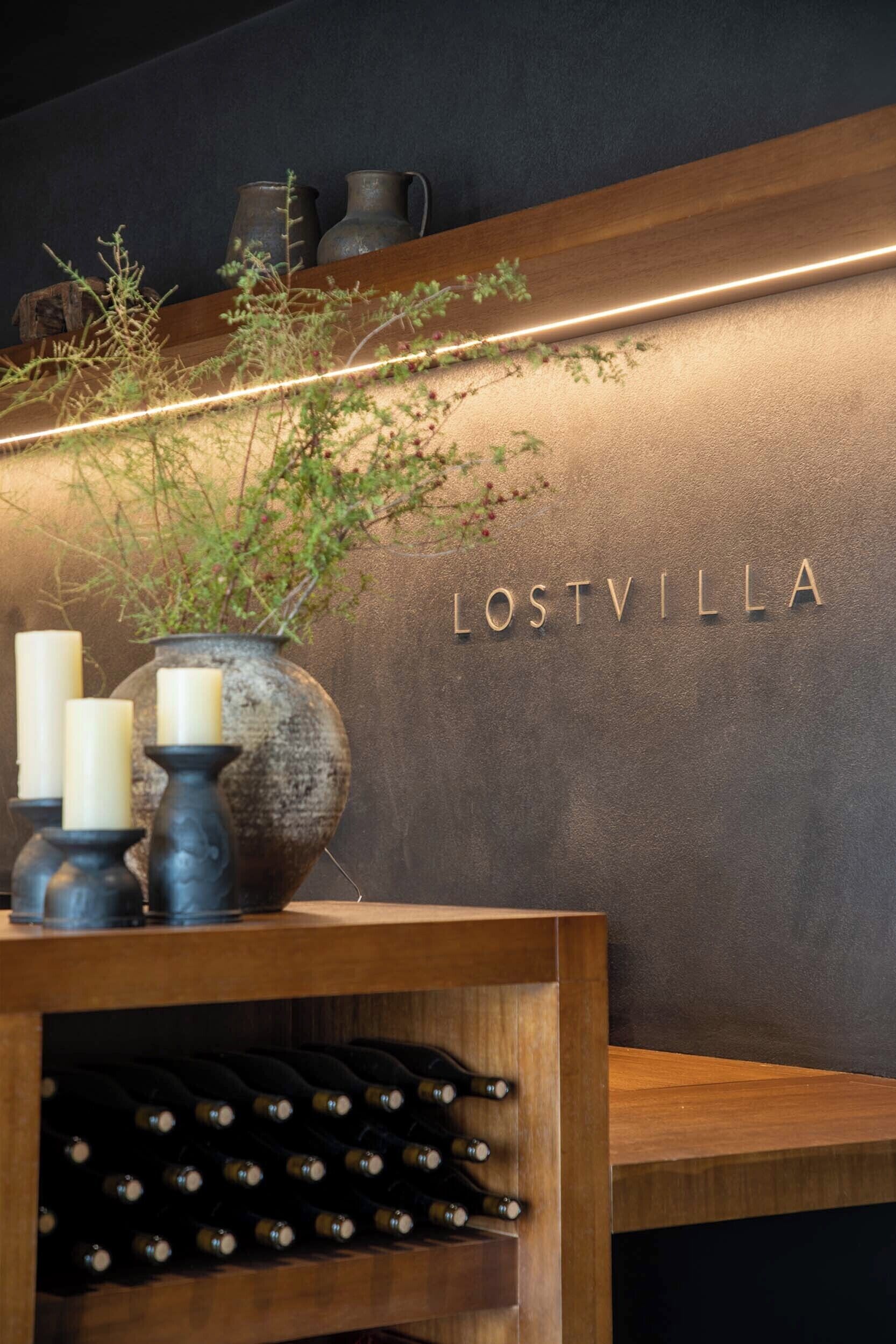 A wooden shelf with candles and a vase, a wine rack below, and the name 'LOSTVILLA' on the wall.