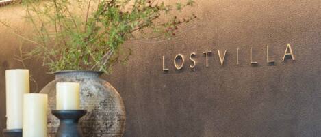 A wooden shelf with candles and a vase, a wine rack below, and the name 'LOSTVILLA' on the wall.