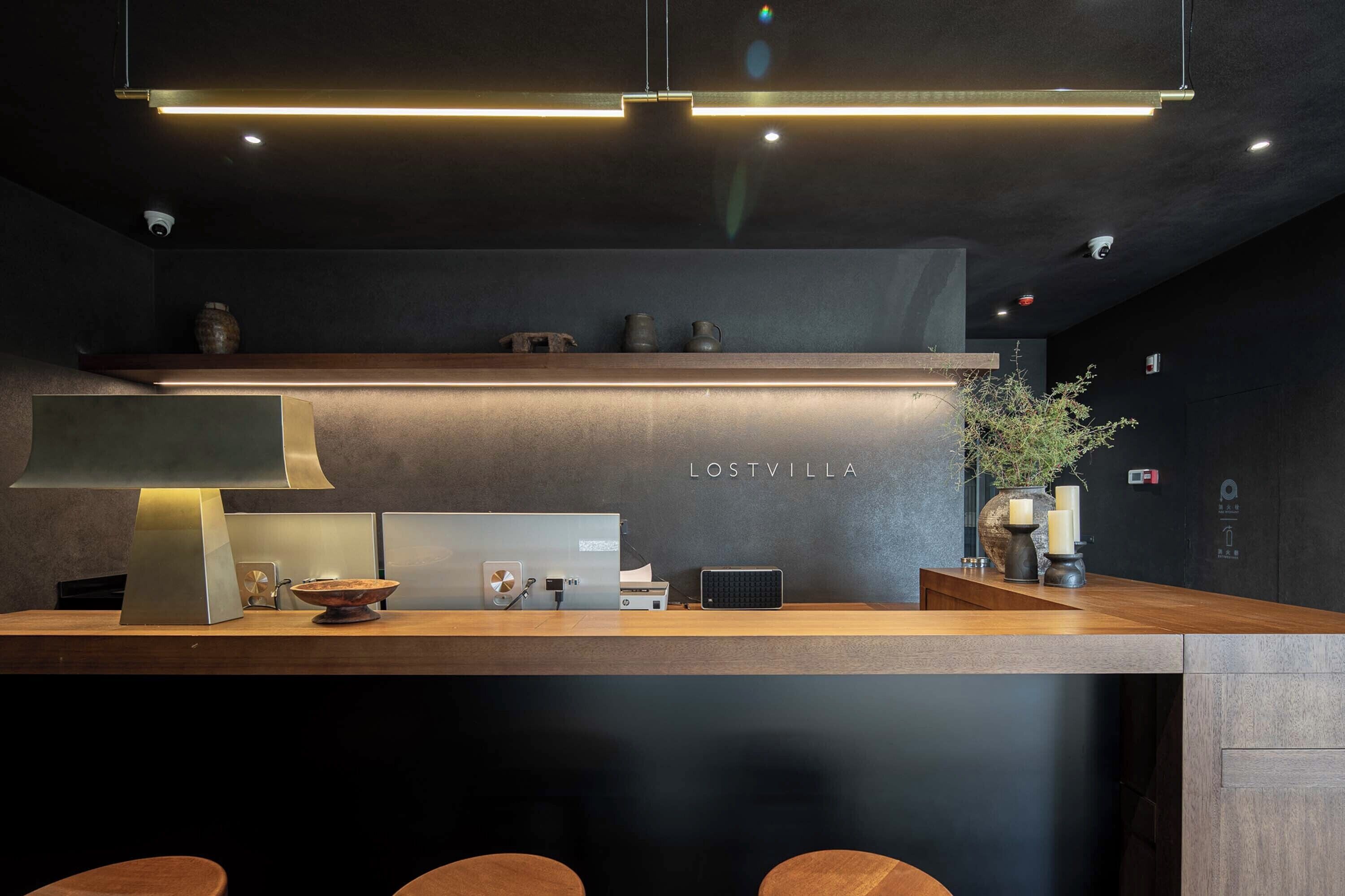 A modern reception desk with a dark wall, a wooden counter, and a sign that reads "LOSTVILLA".