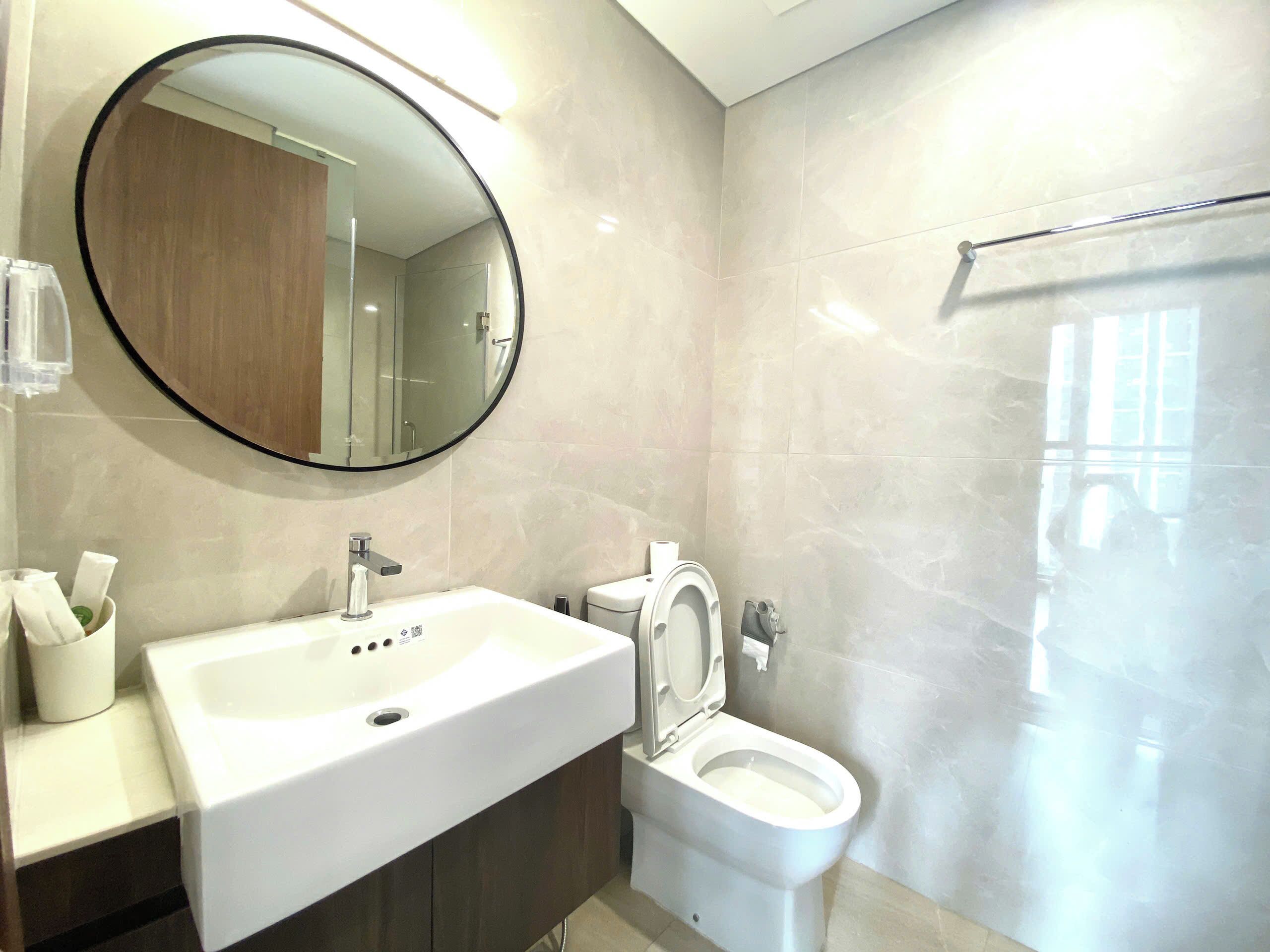 Un baño moderno con un espejo redondo, un lavabo blanco y un inodoro.
