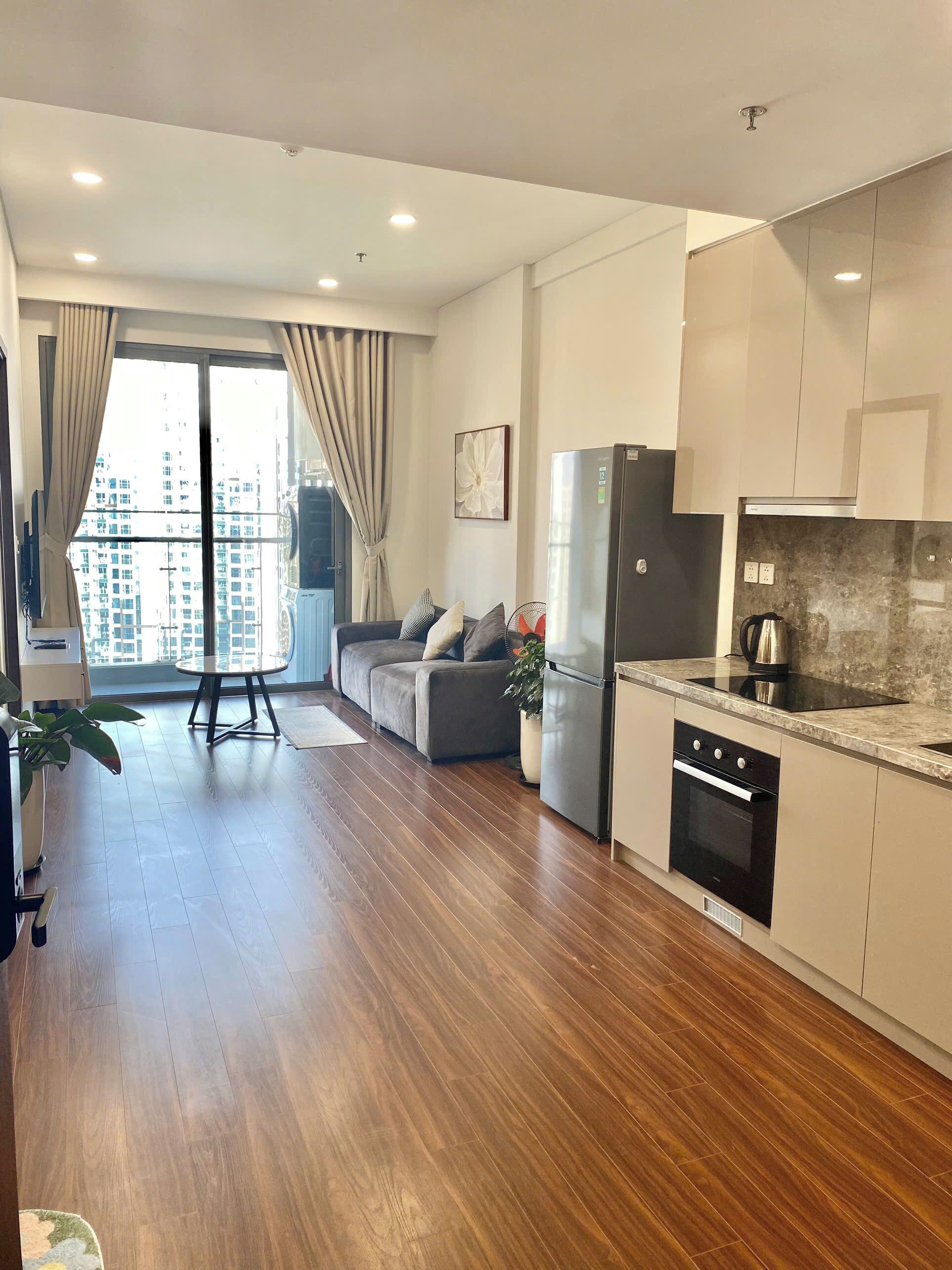 Un appartamento moderno con cucina, zona pranzo e soggiorno. Dispone di pavimenti in legno, un'ampia finestra con tende e vista su edifici alti.