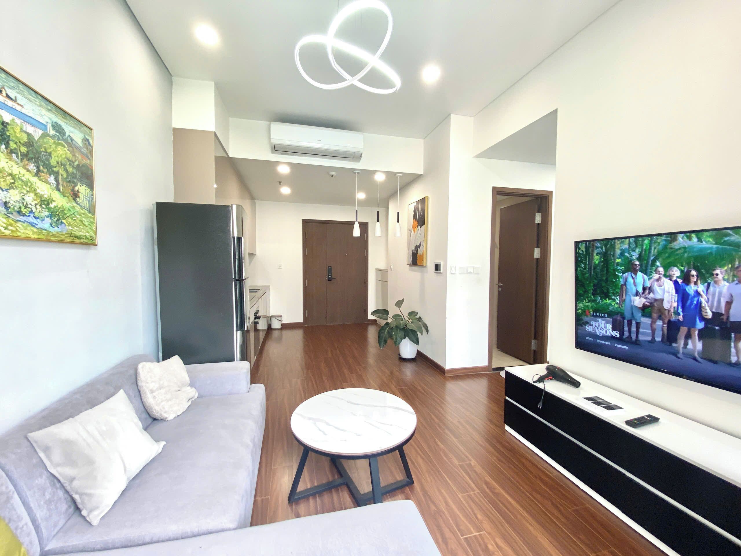 A modern living room with a grey sofa, a round coffee table, a flat-screen TV, and a potted plant.