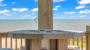 Eine Holzterrasse mit Tisch und Stühlen mit Blick auf einen Strand und klarem Himmel.