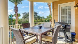 Une terrasse extérieure aménagée avec des meubles en osier, un barbecue et une vue sur des palmiers et une végétation luxuriante.