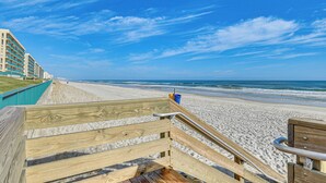 Une promenade en bois qui mène à une plage, avec un ciel bleu dégagé.