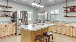 A modern kitchen with granite countertops, stainless steel appliances, wooden cabinets, and a central island with stools. - 4,800-Sq-Ft Cabin w/ Creek Access in Caulfield (Caulfield)