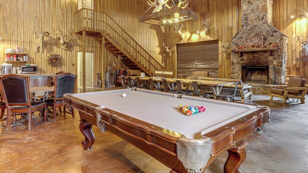 A wooden interior with a pool table, chairs, a fireplace, and a staircase. - 4,800-Sq-Ft Cabin w/ Creek Access in Caulfield (Caulfield)