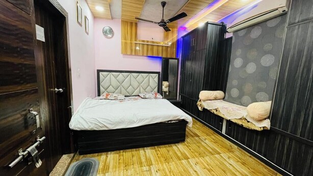 A bedroom with a bed, a bench, a ceiling fan, and a wall clock. - Amrit Residency (Vrindavan)