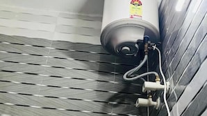 A water heater mounted on a tiled wall with a control valve and a flexible hose. - Amrit Residency (Vrindavan)