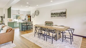 Eine moderne Küche mit Kochinsel, ein Essbereich mit Holztisch und Metallstühlen sowie ein Wohnzimmer mit Ledersofa.