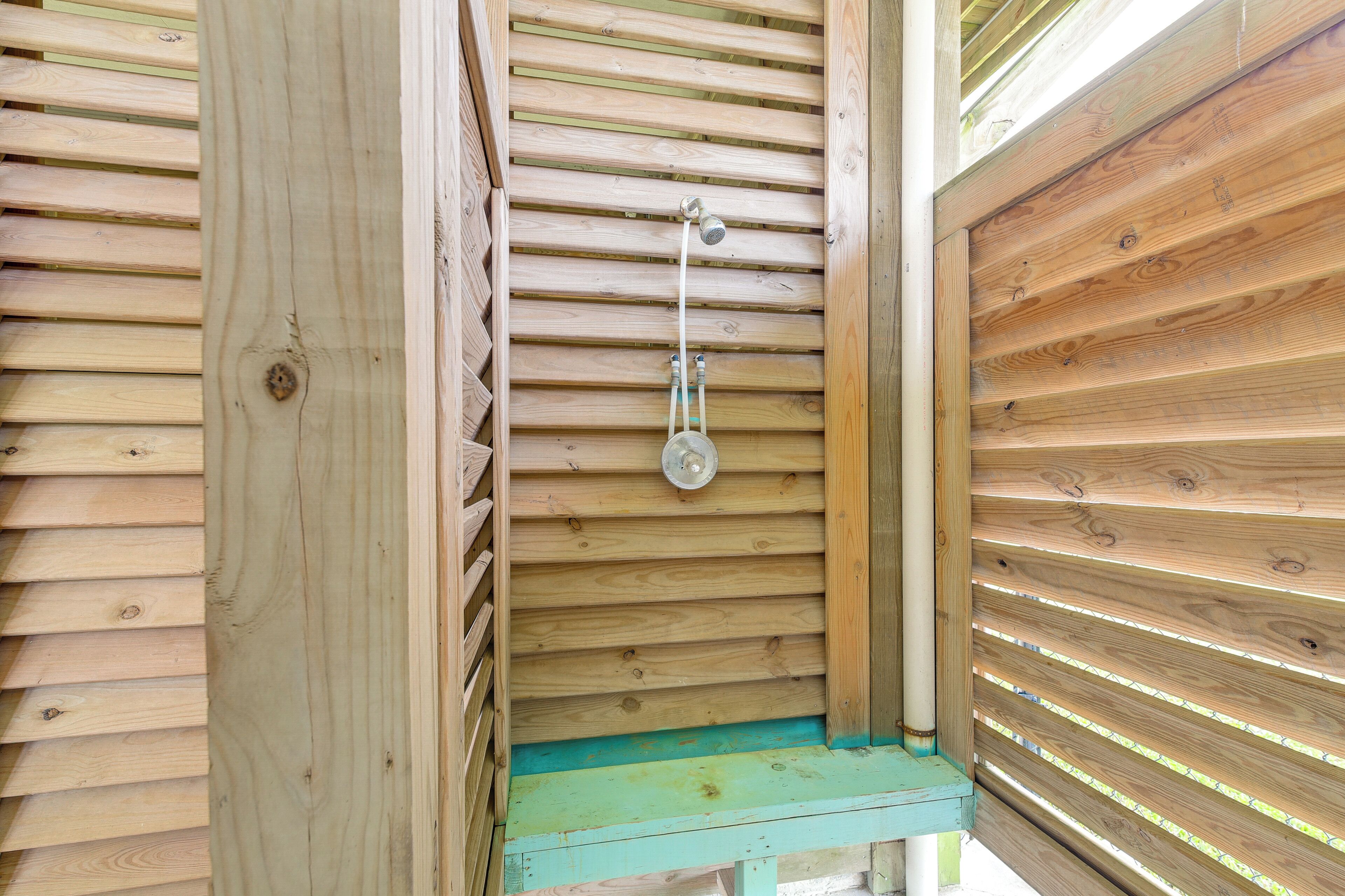 Un espace de douche en bois, doté d’un pommeau de douche en métal et d’un marchepied vert.