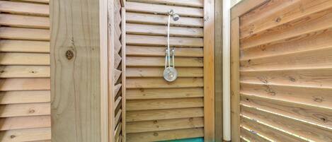 Un espace de douche en bois, doté d’un pommeau de douche en métal et d’un marchepied vert.