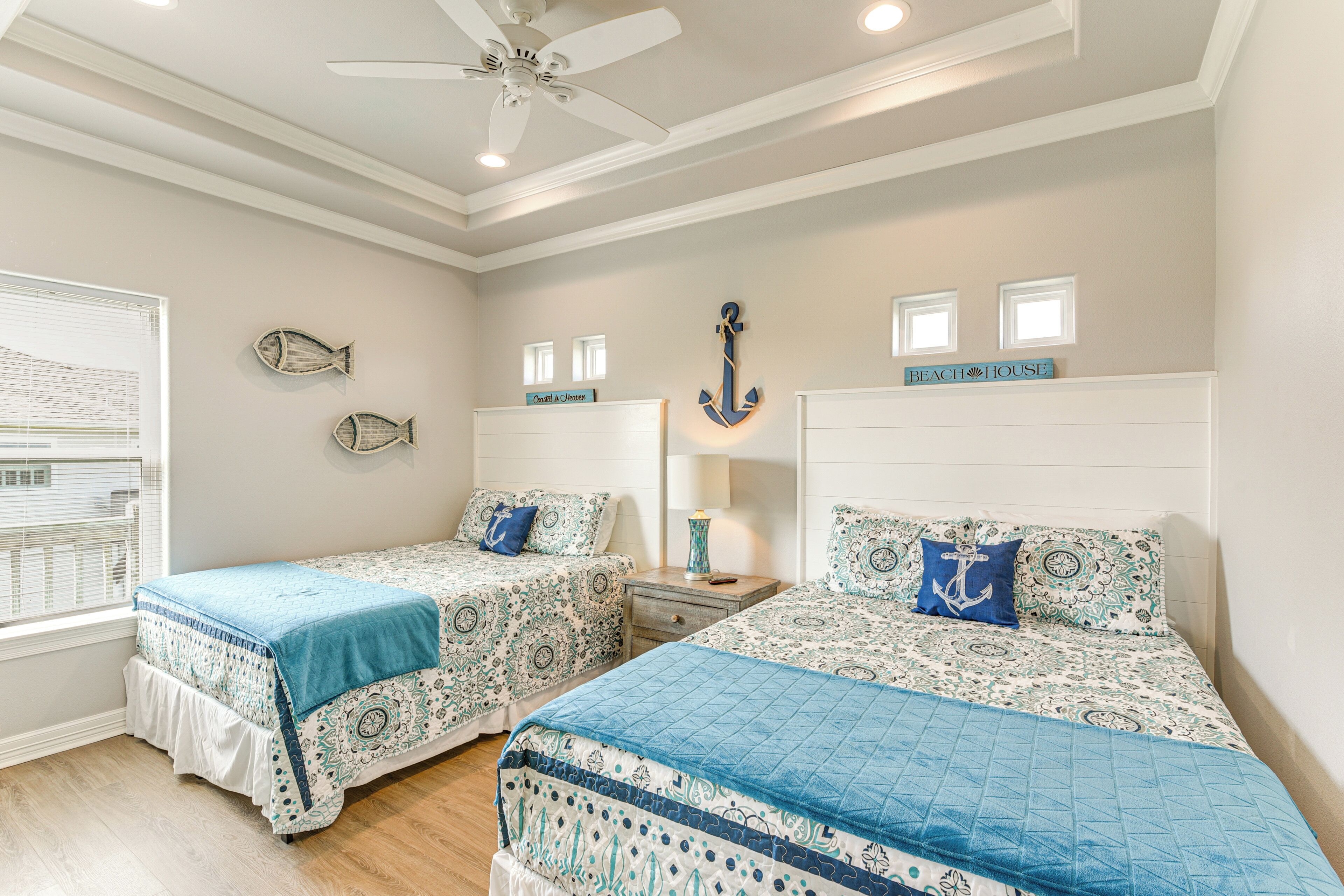 A bedroom with two beds, a ceiling fan, and decorative fish and anchor wall art.