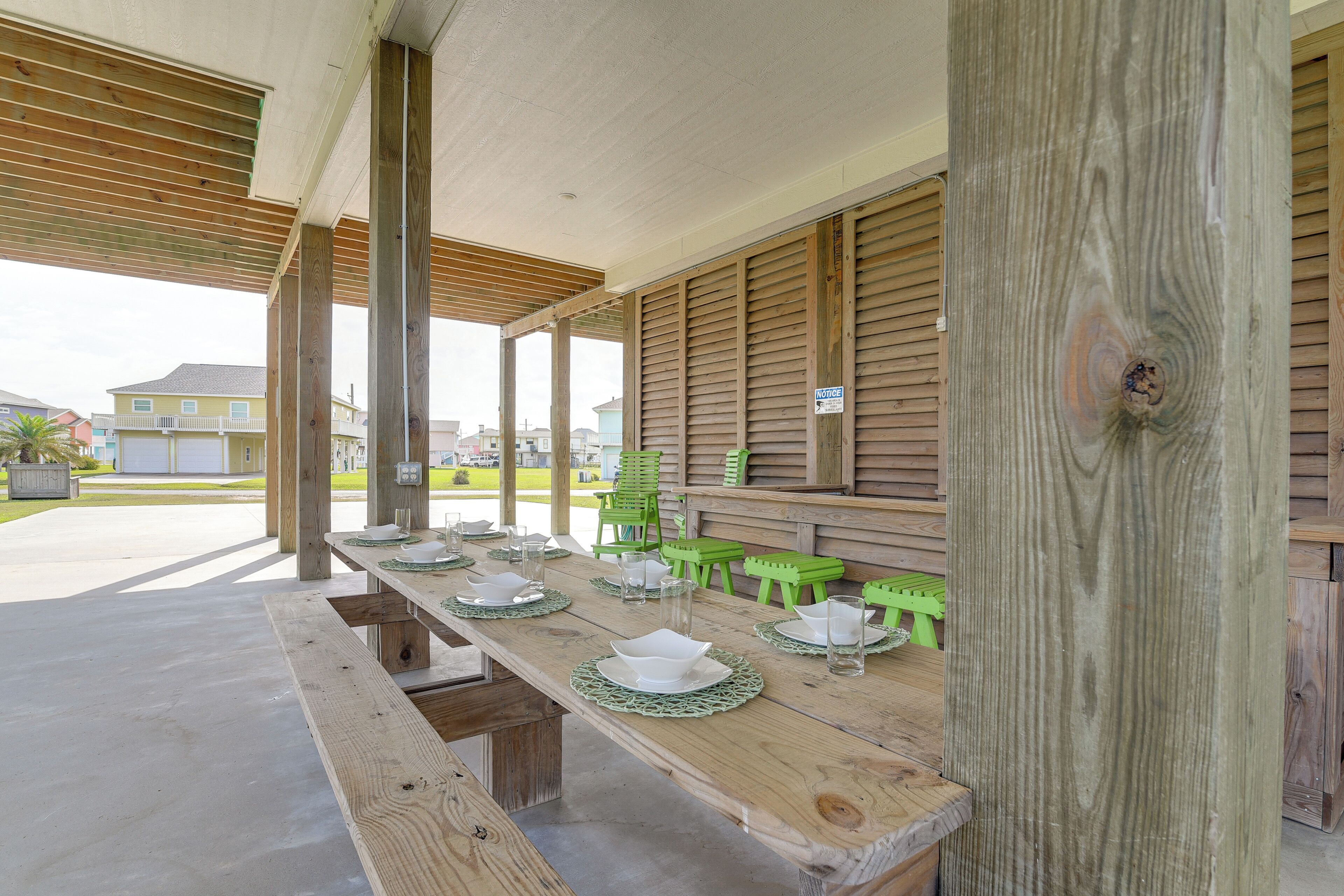 A covered outdoor dining area with wooden tables and benches, a view of houses in the background, and a 'No Smoking' sign on the wall.