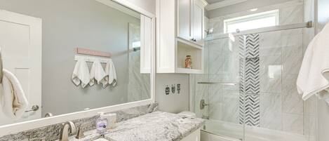 Un baño moderno con un lavamanos de mármol, ducha con cerramiento de vidrio y tocador con cajones.