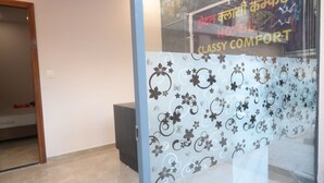 A szálloda recepciója üvegfallal van elválasztva, melyen virágminták láthatók, és egy „HOTEL CLASSY COMFORT” feliratú tábla található rajta.