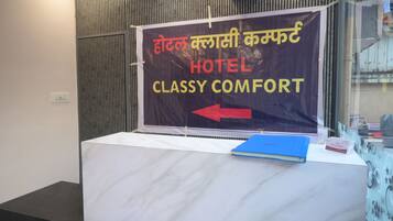 Una mesa de recepción con un letrero que indica 'HOTEL CLASSY COMFORT' y una flecha señalando a la izquierda.
