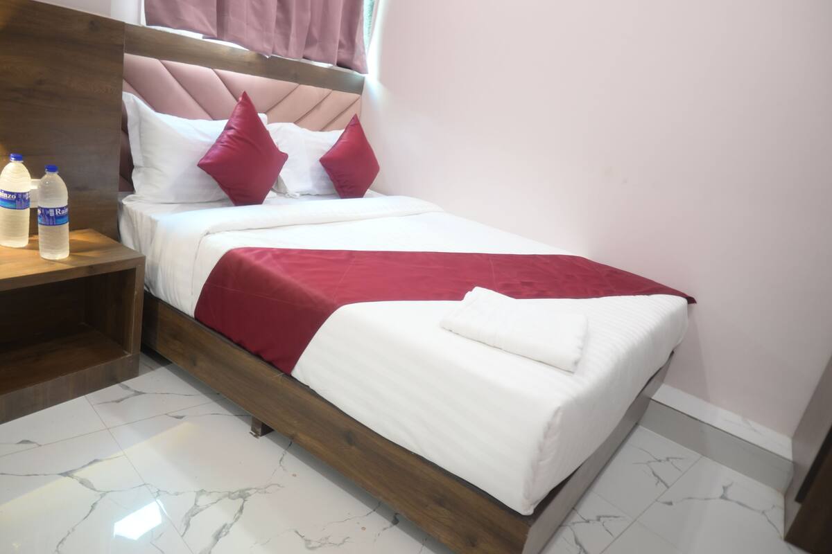 A neatly made bed with a wooden headboard, white and red bedding, and a red throw blanket.