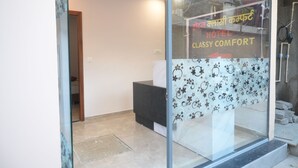 Egy üvegajtós, recepciós pulttal és egy felsőbb szintre vezető lépcsővel ellátott szállodai recepcióny.