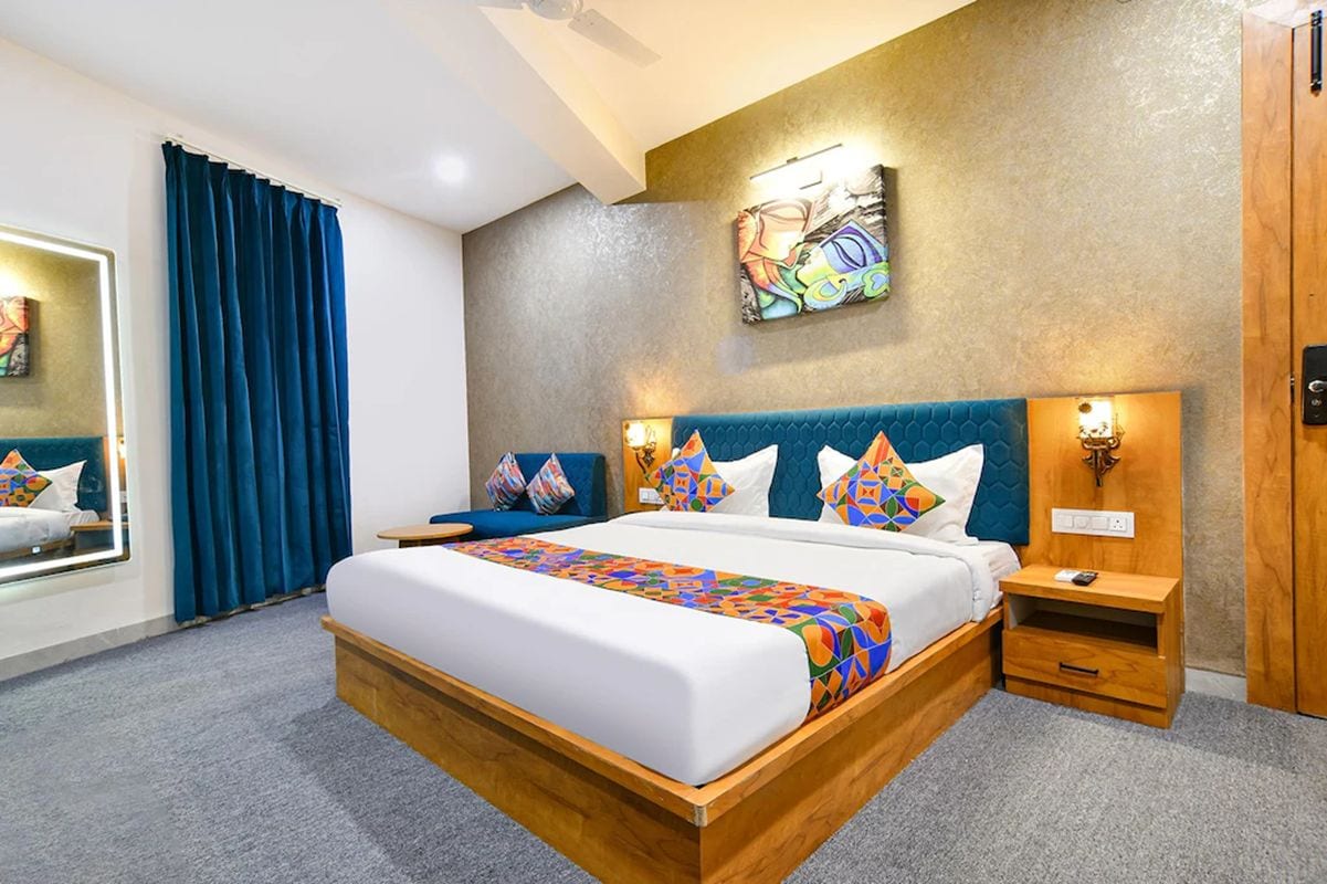 A hotel room with a large bed, a nightstand, a wall-mounted artwork, and a window with curtains.