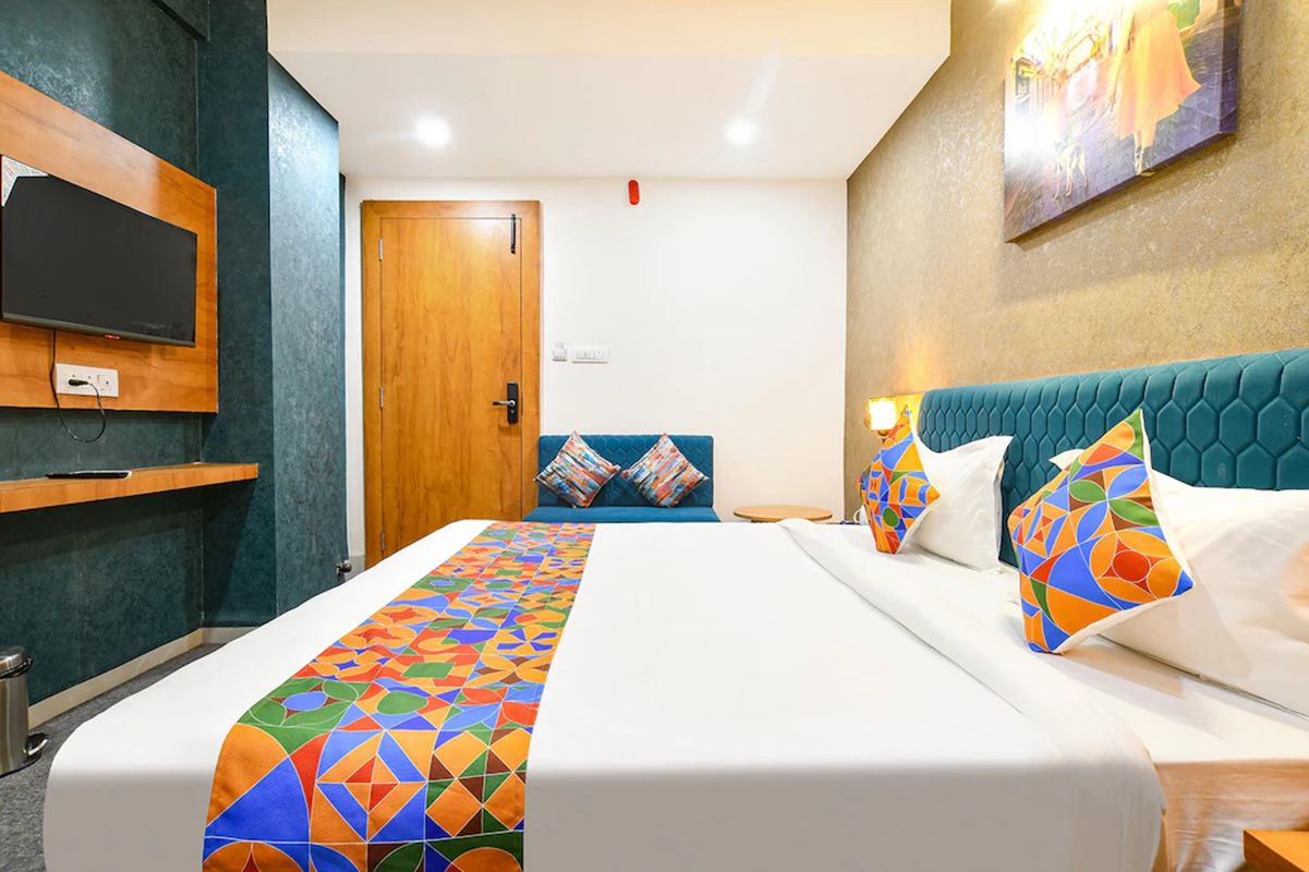 Une chambre d’hôtel avec un lit, un téléviseur fixé au mur, une porte et un tableau accroché au mur.