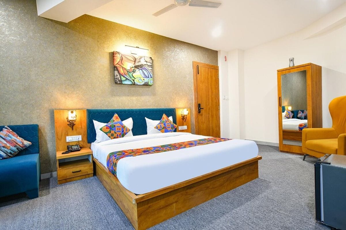 Habitación de hotel con una cama grande, cabecera de madera, dos mesitas de noche con lámparas, un sofá azul, un armario de madera y un ventilador de techo.