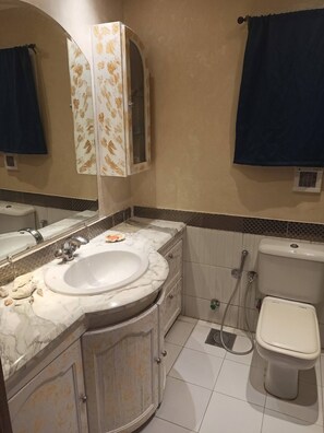A bathroom with a white sink, a mirror, a toilet, and a shower. - Welcoming 3-bedroom apartment with AC in vibrant Cairo Governorate (Cairo Governorate)