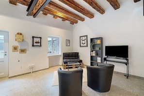 Un salon comprenant un canapé, un pouf, des poutres en bois, un téléviseur et des tableaux encadrés accrochés au mur.