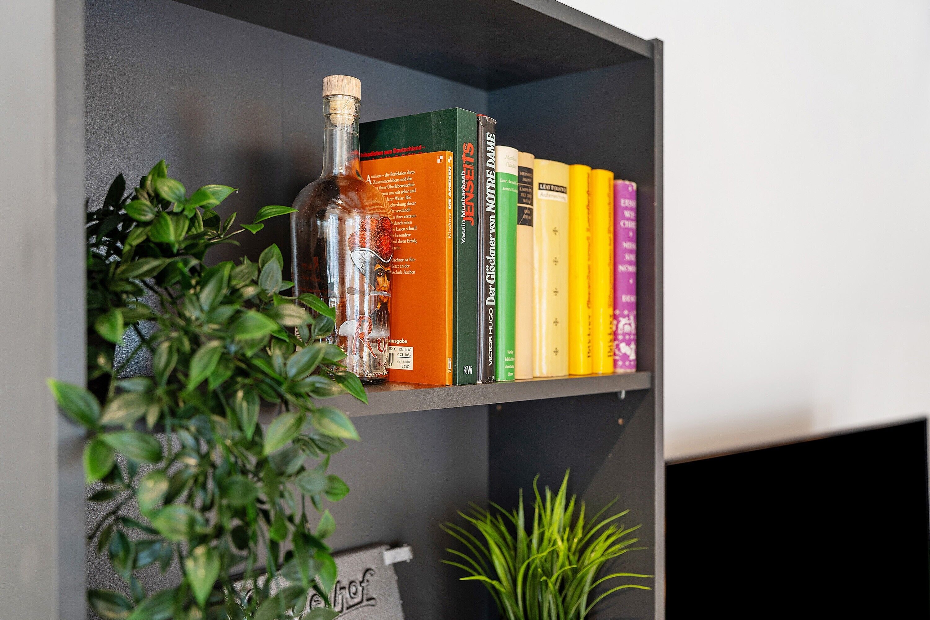 A bookshelf with books and a bottle.