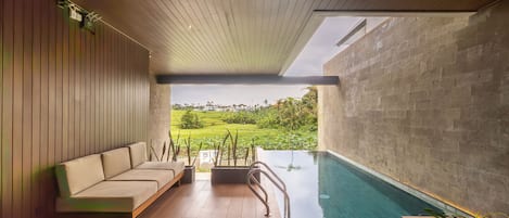 Un área de piscina interior moderna con techo de madera, un sofá y vista a un paisaje exuberante.