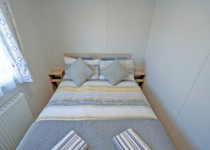 A small, neatly arranged bedroom with a bed, two pillows, a bedside table, and a radiator. - 1 bedroom accommodation in Millom (Millom)