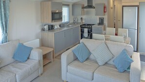 Ett kompakt bostadsutrymme med ett litet kök, två soffor med kuddar och en matplats.