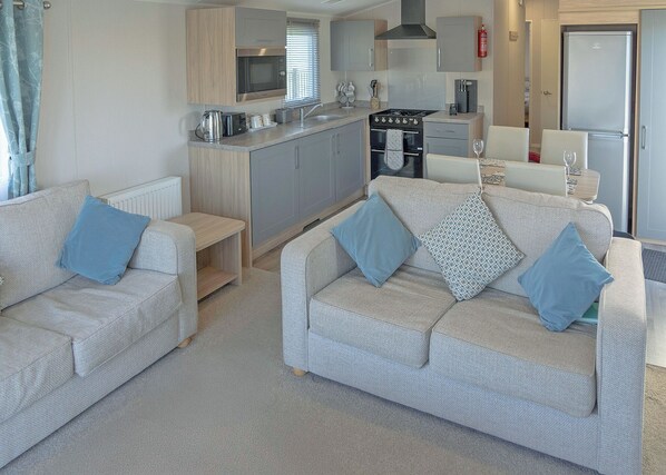 A compact living space with a kitchenette, two sofas with cushions, and a dining area. - 3 bedroom accommodation in Millom (Millom)