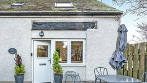 Una casa amb façana blanca, una porta amb finestreta i un rètol que diu 'The Coach House', i mobles d'exterior com una taula i cadires.