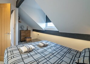Un dormitorio con techo inclinado, un armario de madera, una mesita de noche y una cama con colcha estampada.