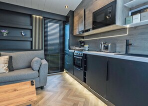 A modern kitchen with a built-in microwave, toaster, and oven, a grey sofa, and a wooden herringbone floor.
