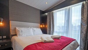 Habitación de hotel con una cama grande, cabecera, mesita de noche, ventana con cortinas y vistas al exterior.