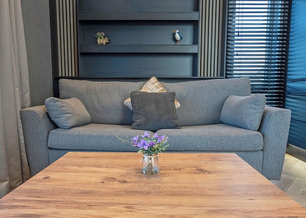 A grey sofa with a vase of purple flowers on a wooden coffee table.