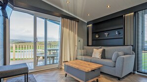 Una sala de estar moderna con un sofá, una mesa de centro de madera y vistas a una terraza y paisaje a través de amplios ventanales.