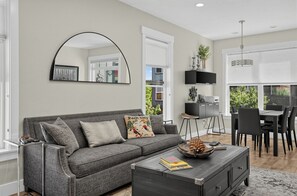 A modern living room with a grey sofa, a coffee table, a TV, and a dining area with chairs and a table. - Rooftop Deck w/ Hot Tub | Near Dining & Ski Slopes | The Lookout by AvantStay (Park City)