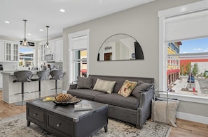 A modern living room with a grey sofa, a coffee table, and a large window with a view of the street. - Rooftop Deck w/ Hot Tub | Near Dining & Ski Slopes | The Lookout by AvantStay (Park City)