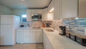 A modern kitchen with white cabinets, a stainless steel microwave, and a coffee maker. - 2 Cozy Cottages | Private Yards, Fire Pit, Walkable Location in Spanish Village (Port Aransas)