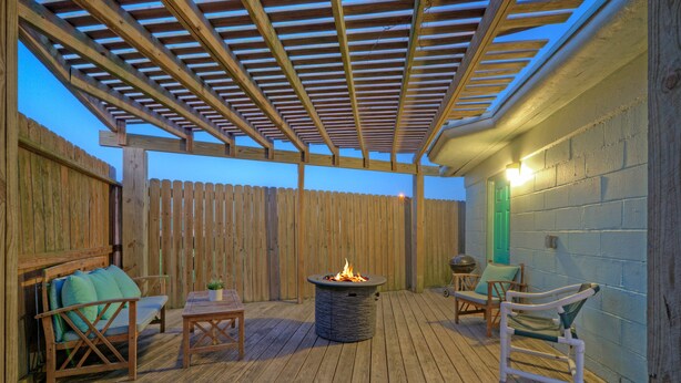 An outdoor deck with a fire pit, wooden furniture, and a wooden fence. - 2 Cozy Cottages | Private Yards, Fire Pit, Walkable Location in Spanish Village (Port Aransas)