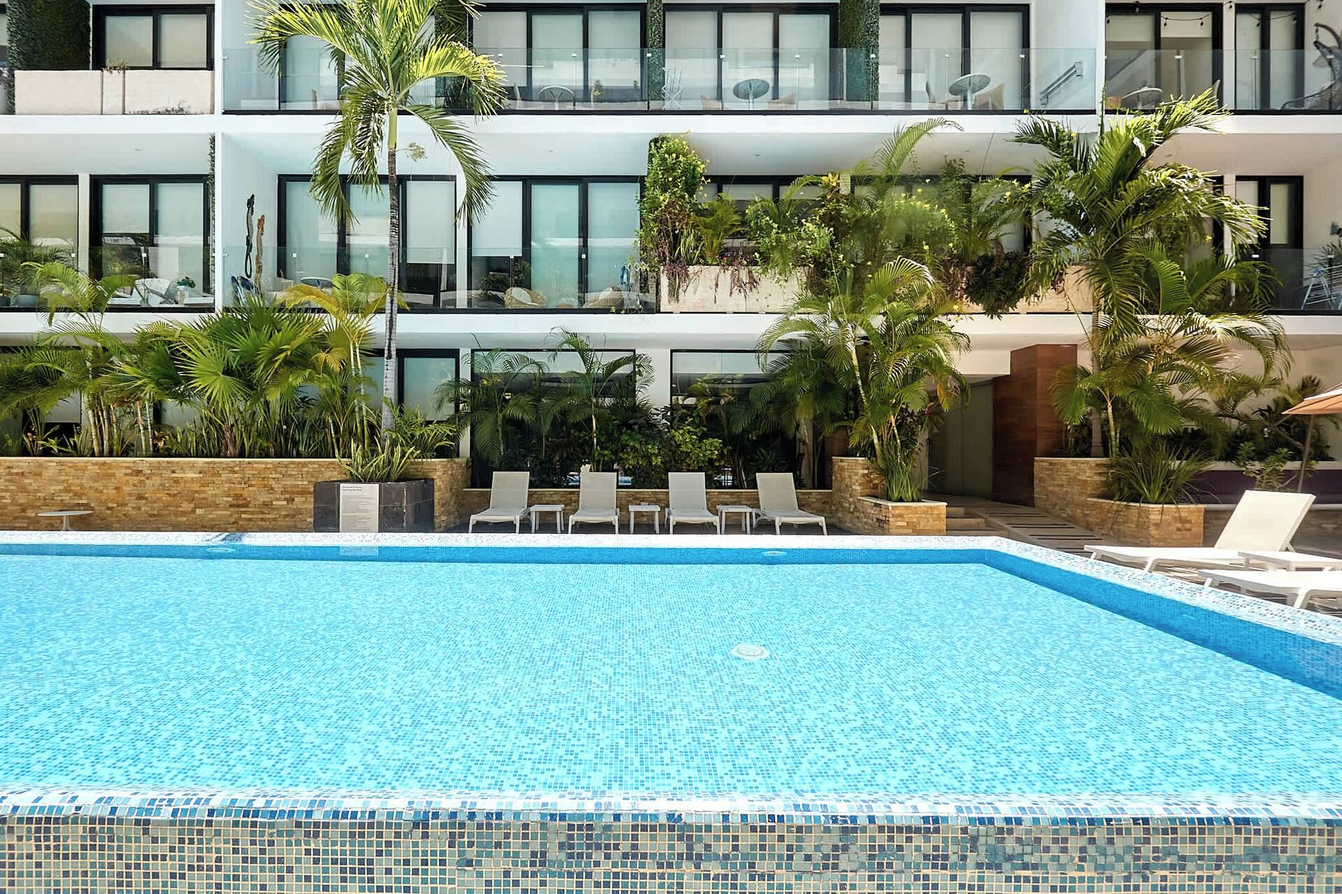 Un hotel moderno con piscina, poltrone relax e rigogliosa vegetazione tropicale.