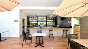 A restaurant with a bar area, wooden flooring, and black chairs. - 2BR condo w/ pools, gym & balcony, steps to beach (Playa del Carmen)