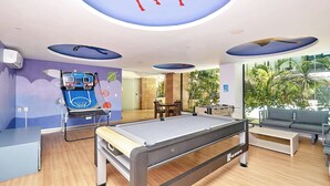 A modern indoor recreational area with a pool table, a basketball hoop, and a seating area with a view of palm trees. - 2BR condo w/ pools, gym & balcony, steps to beach (Playa del Carmen)